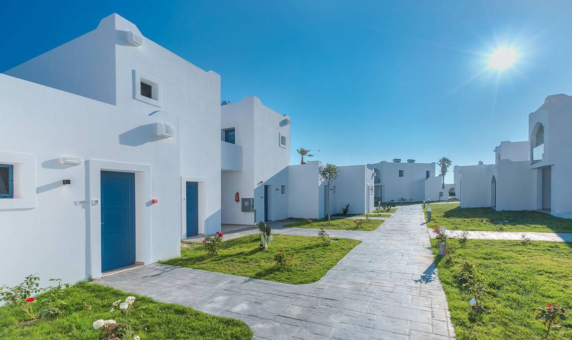 Aeolos Beach Hotel in Kos, Außenbereich mit weißen Gebäuden und blauen Türen an einem sonnigen Tag.