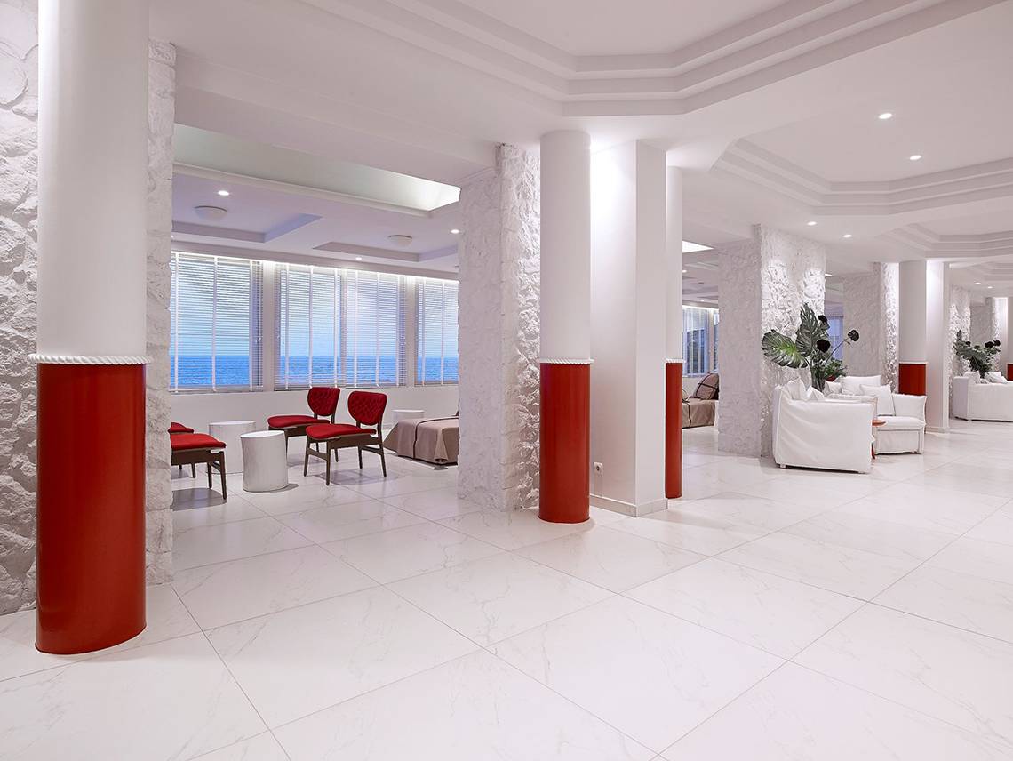 Innenbereich des Dimitra Beach Hotel & Suites mit weißen Böden, roten Säulen und Blick aufs Meer