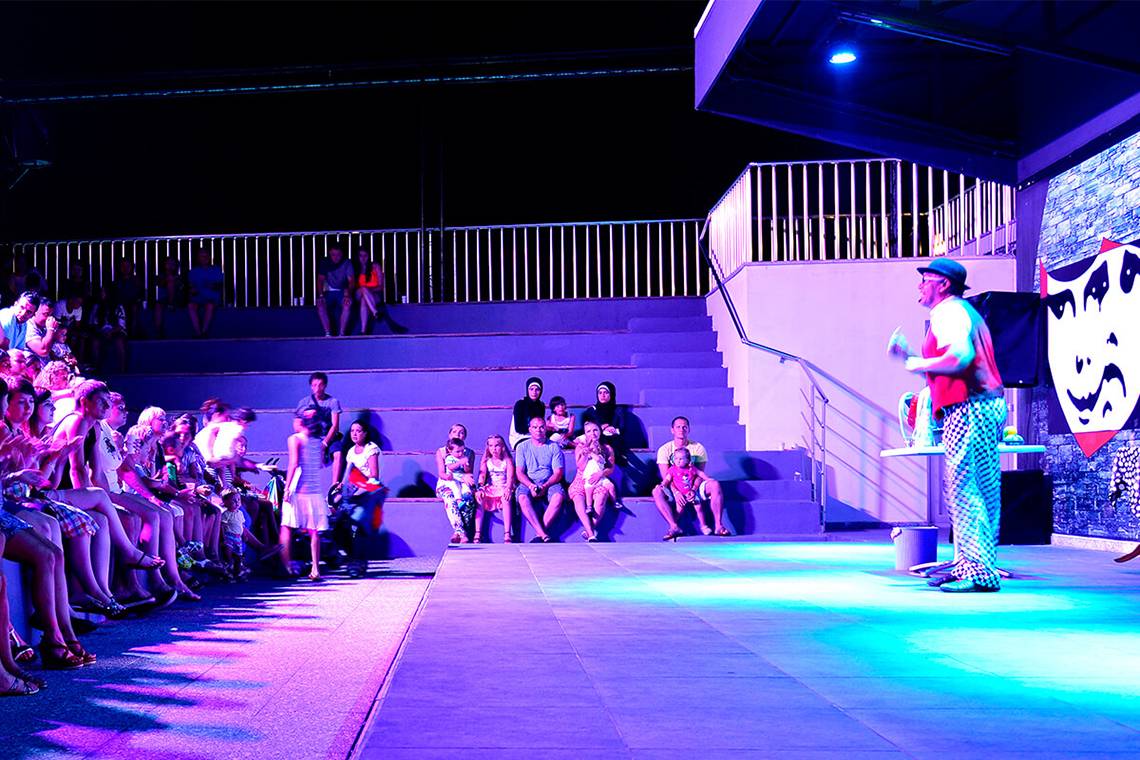 Abendveranstaltung im White City Resort mit einem Clown auf der Bühne und Publikum auf den Stufen.