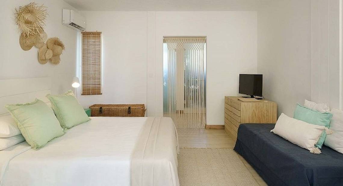 Schlafzimmer im The Ravenala Attitude Hotel mit weißen Wänden, einem großen Bett, grünen Kissen und einer Couch.