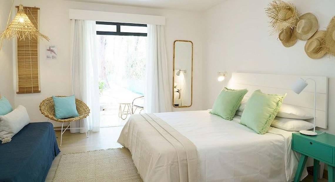 Schlafzimmer im Ravenala Attitude Hotel mit weißen Wänden, einem großen Bett, grünen Kissen, einem Nachttisch und einem Spiegel.
