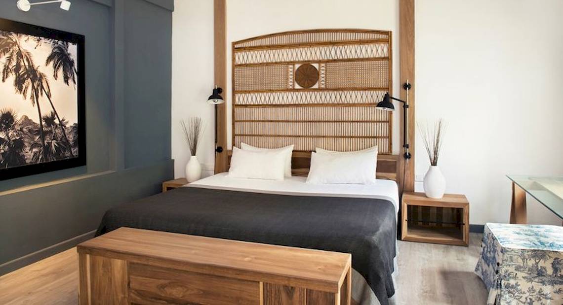 Ein modernes Hotelzimmer mit einem großen Bett, einem hölzernen Kopfteil, zwei Nachttischen und einer Gemäldewand.