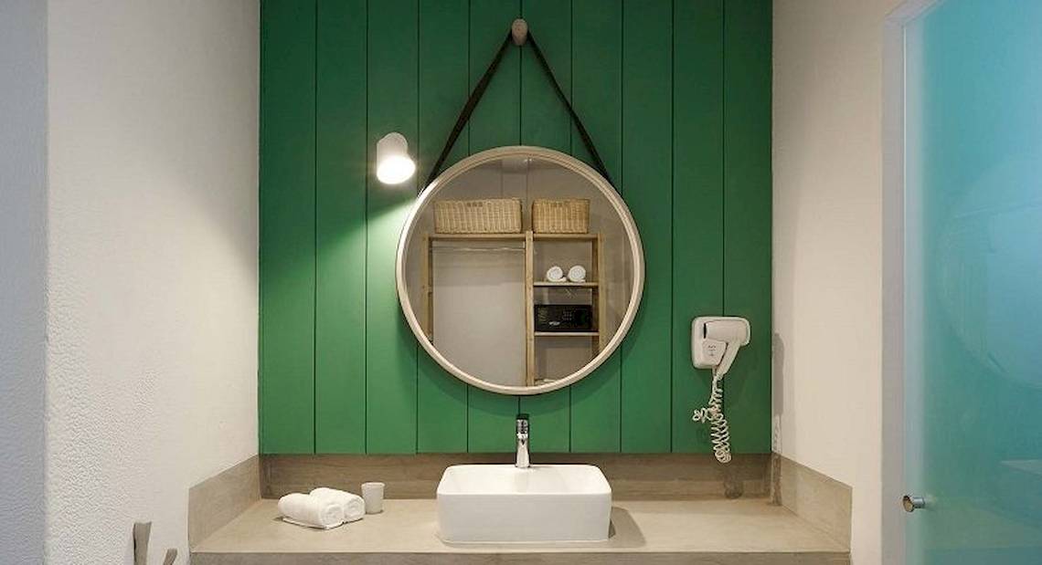 Badezimmer im The Ravenala Attitude Hotel mit grünen Wänden, einem runden Spiegel und einem weißen Waschbecken.
