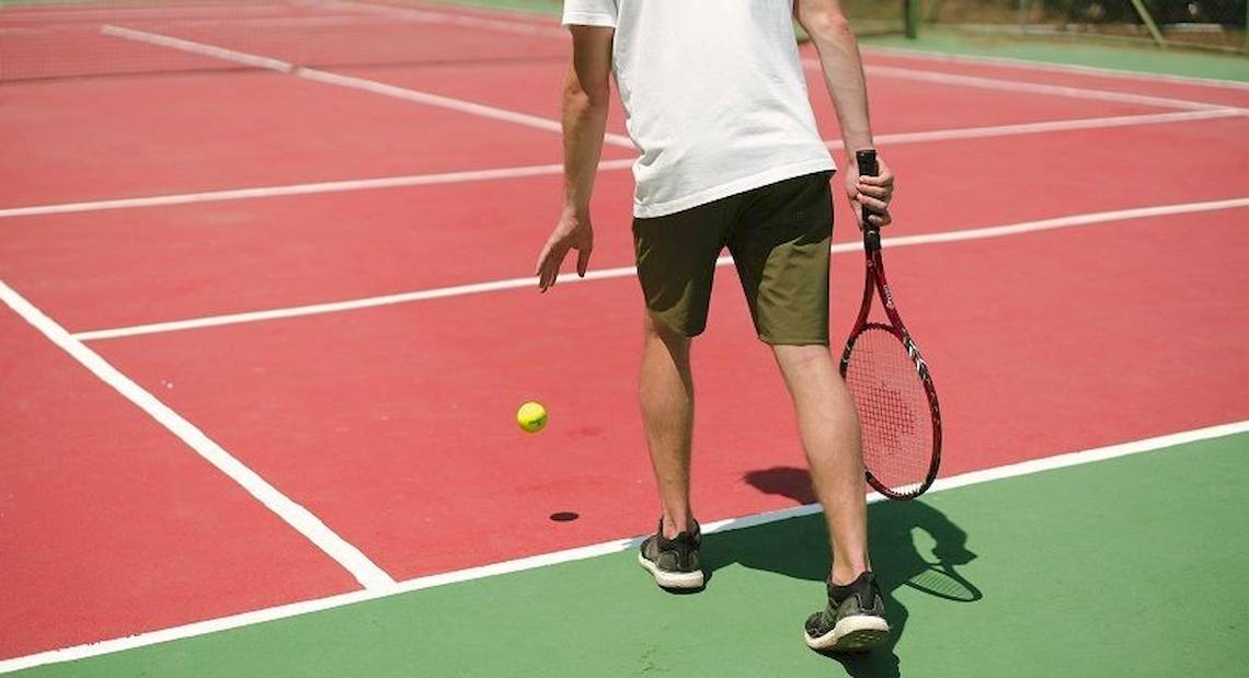 Ein Tennisspieler auf einem roten Tennisplatz, bereit, einen Ball zu schlagen.