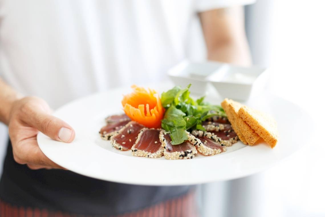 Teller mit Fisch, Salat und Brotstücken, von einer Person gehalten.
