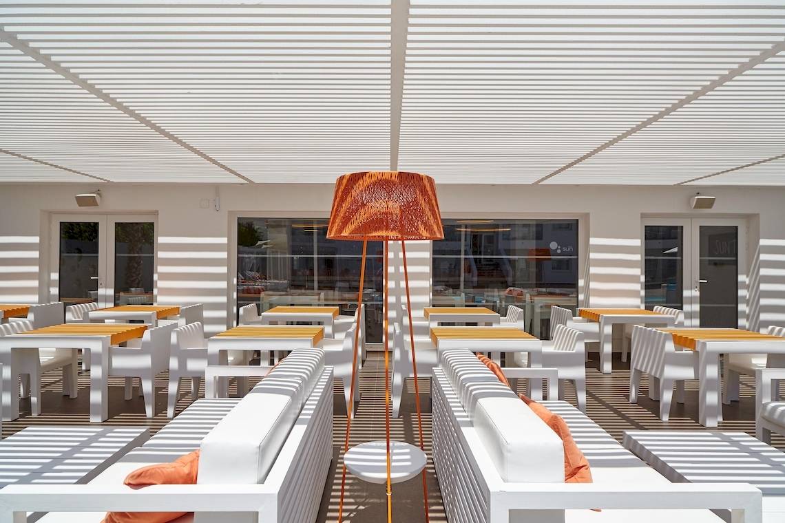 Terrasse des Ibiza Sun Apartments mit weißen Möbeln und orangefarbenen Kissen.