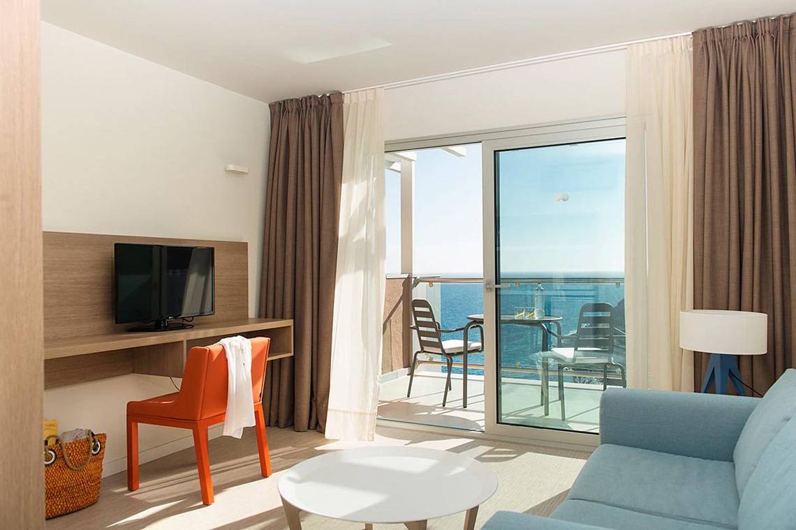 Zimmer mit Meerblick im Riviera Vista Hotel, ausgestattet mit Fernseher, Schreibtisch und Balkonmöbeln.