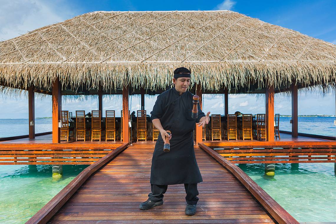 Ein Mitarbeiter des Kurumba Maldives Hotels steht auf der Terrasse und lächelt in die Kamera.