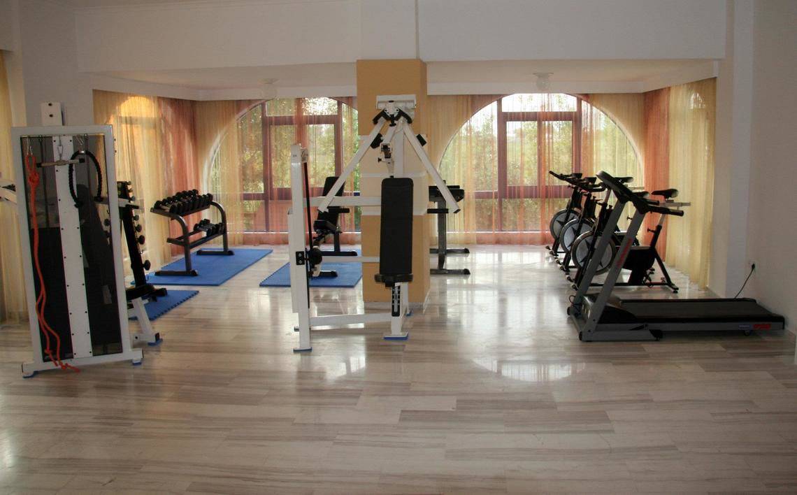 Fitnessraum im Hotel Gaia Village mit verschiedenen Trainingsgeräten und freien Fenstern.