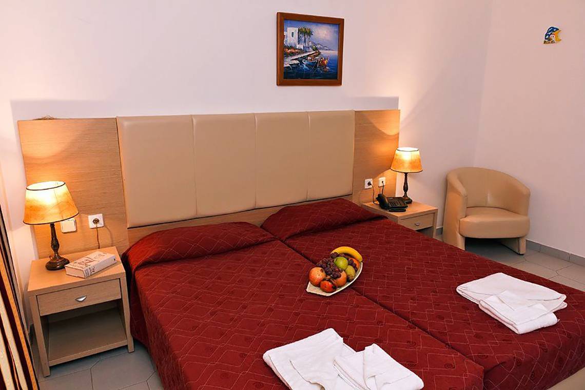 Doppelzimmer im Gaia Village Hotel mit zwei roten Betten, Früchten und Lampen.