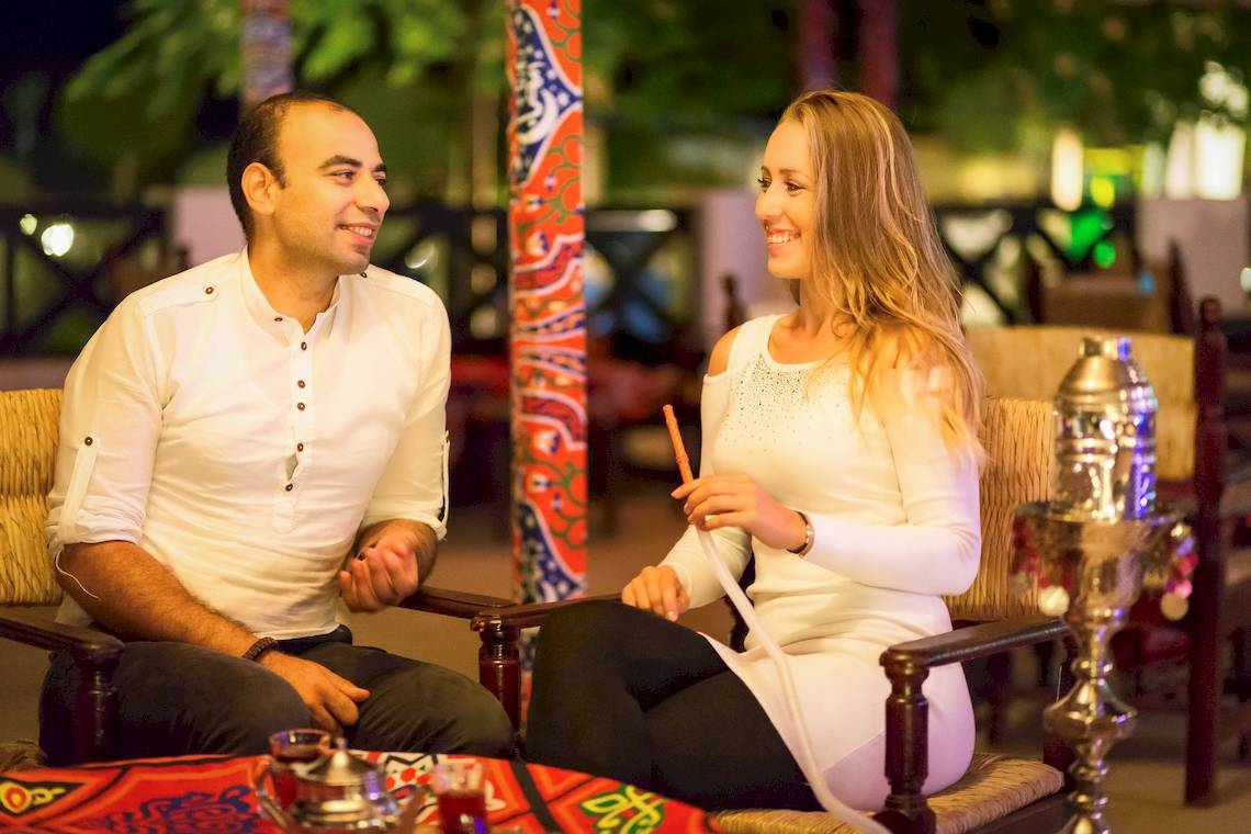 Ein Paar im Hilton Marsa Alam Nubian Resort, das draußen raucht und lächelt.