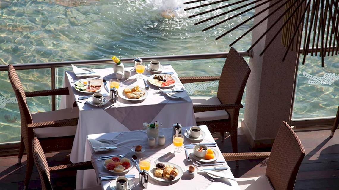 Frühstückstisch am Pool im Sentido Port Royal Villas & Spa mit Blick auf das Wasser.