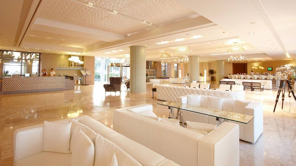 Lobby des Sentido Port Royal Villas & Spa mit weißen Möbeln, Marmorboden und hohen Decken.