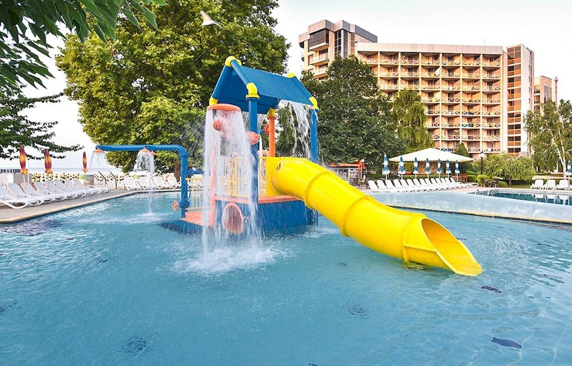 Wasserrutsche im Außenbereich des Kaliakra Beach Hotels mit grünen Bäumen und Gebäude im Hintergrund.