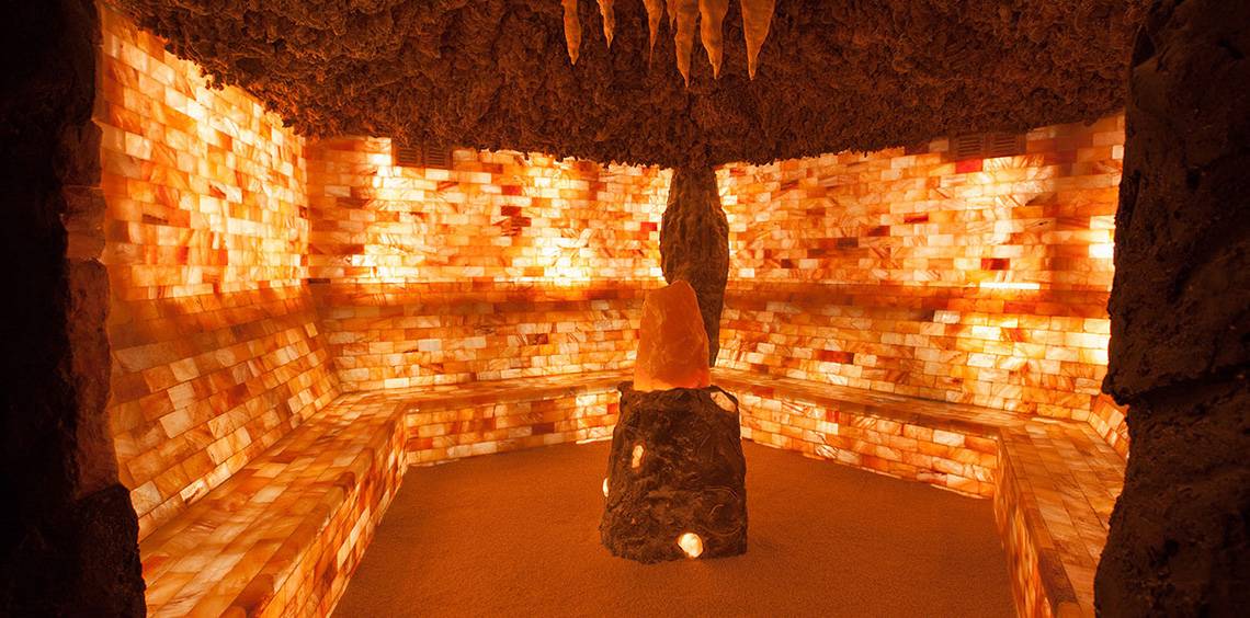 Innenansicht einer Salzkristallsauna im Lopesan Costa Meloneras Resort & Spa mit braunen Bänken und orangefarbenen Wänden.