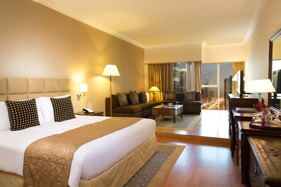 Suite-Zimmer im Millennium Plaza Downtown Hotel mit Bett, Sofa, Schreibtisch und Stadtblick.