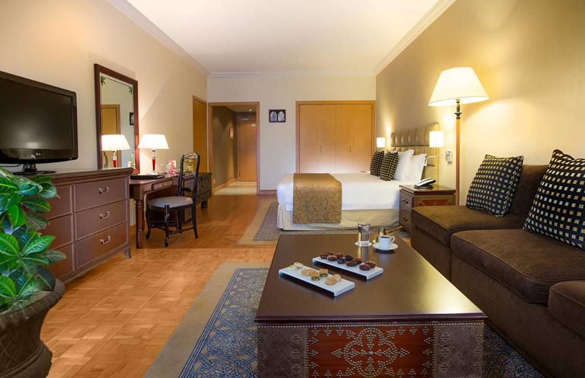 Innenansicht einer Hotelsuite im Millennium Plaza Downtown mit Bett, Wohnzimmer und Schreibtisch.