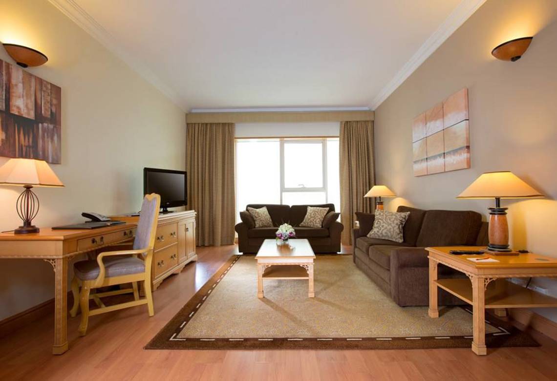Wohnzimmer im Millennium Plaza Downtown Hotel mit zwei Sofas, Tisch, Fernseher und Lampen.
