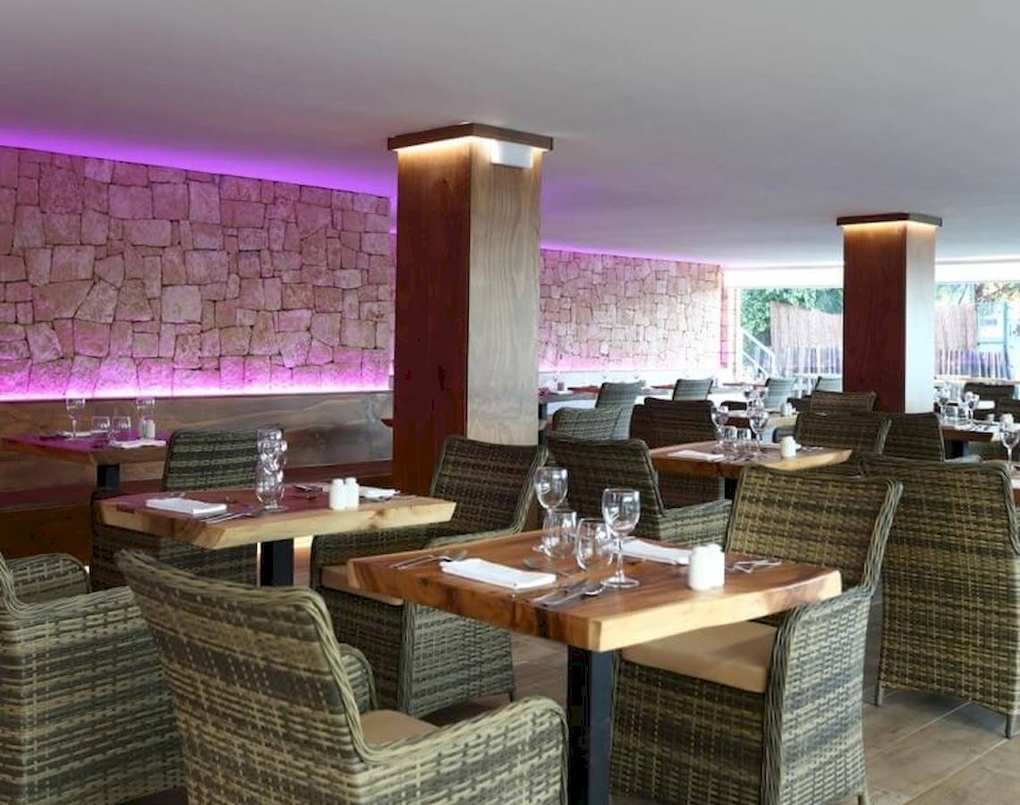Innenansicht des Restaurants im Sandos El Greco Beach Hotel mit steinerner Wand und lila Beleuchtung.