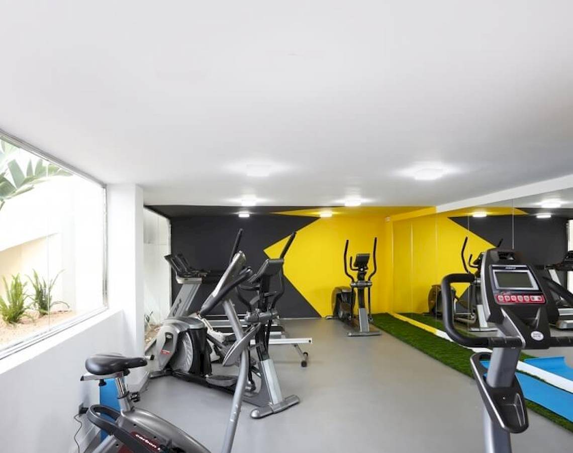 Fitnesscenter-Innenbereich im Sandos El Greco Beach Hotel mit Cardiogeräten und einer Fensteransicht.