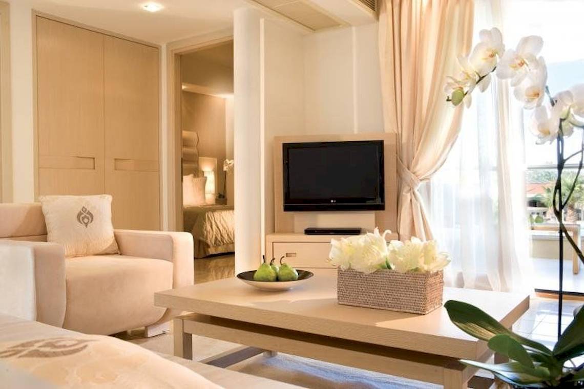 Wohnzimmer des Porto Sani Hotels mit Fernseher, Sofa, Tisch und Blumen.