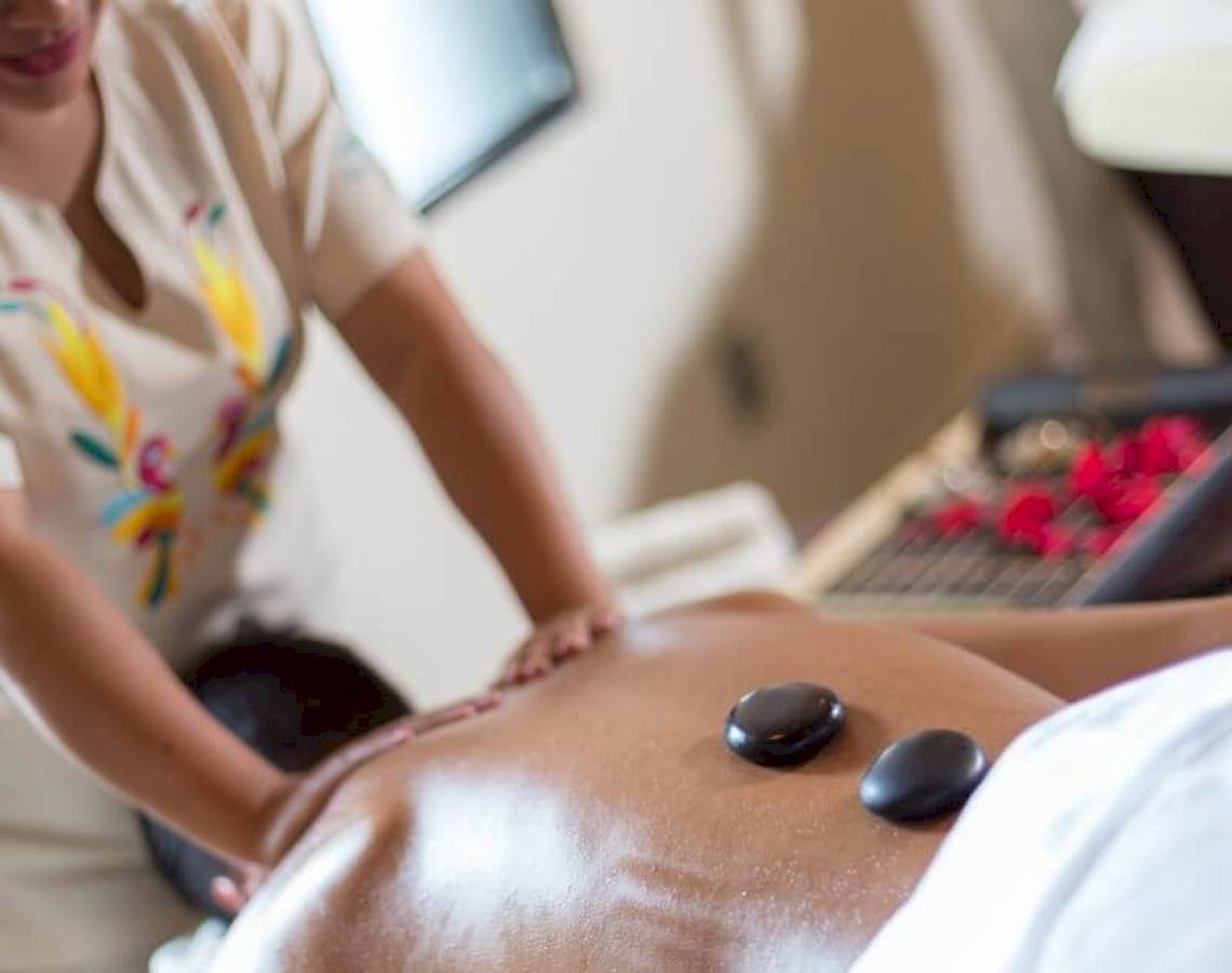 Eine Massagebehandlung im Sandos Caracol Eco Resort, bei der eine Person mit schwarzen Steinen auf dem Rücken liegt.
