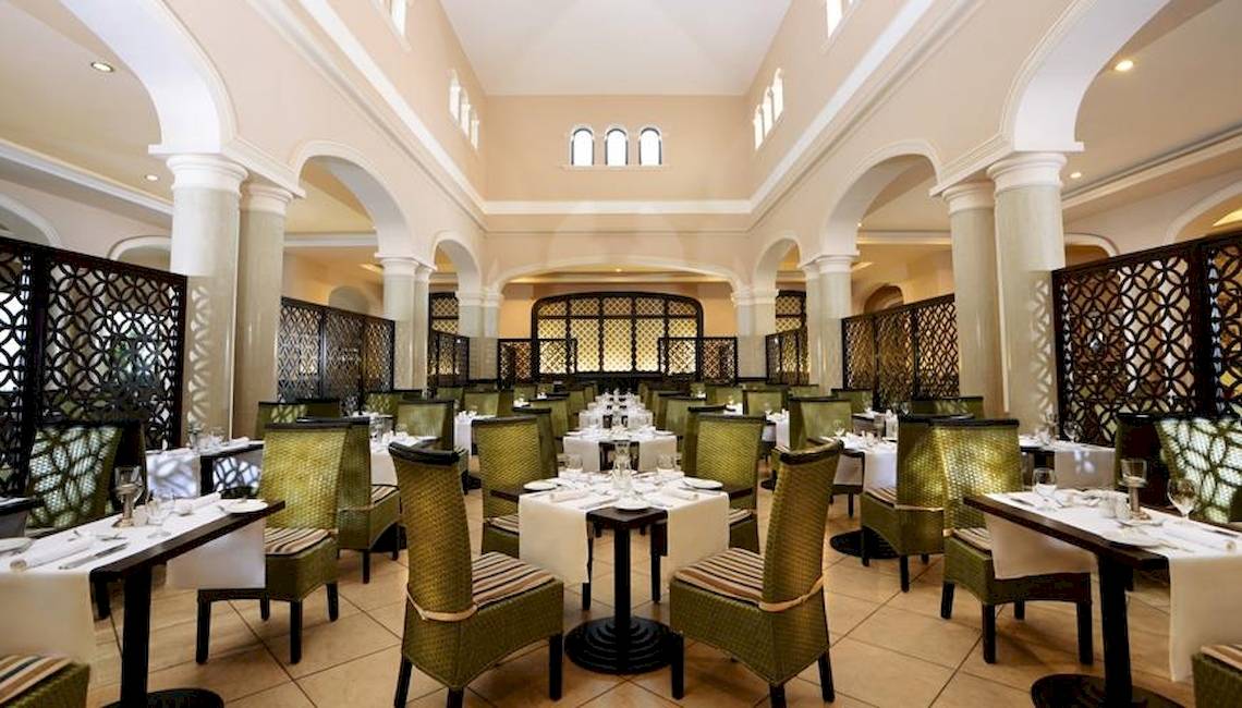 Innenansicht des Restaurants im Jaz Aquamarine Resort mit runden Tischen und Stühlen.