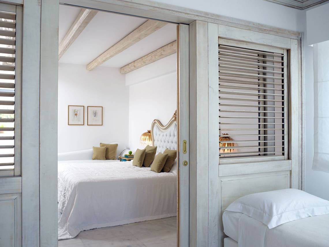 Innenansicht eines Schlafzimmers im Mitsis Laguna Resort mit einem Bett, Kissen und dekorativen Elementen.