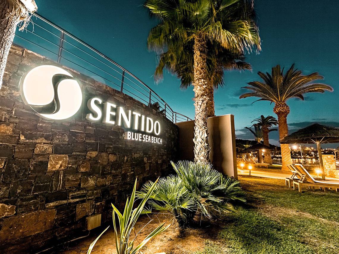 Das Eingangsschild des Sentido Blue Sea Beach Hotels bei Nacht, mit Beleuchtung und Palmen im Vordergrund.