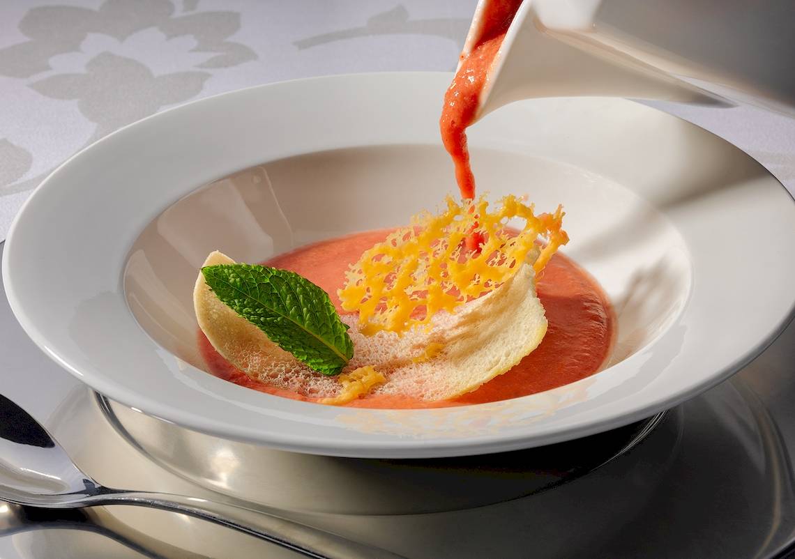 Ein Gericht mit Tomatensuppe in einer weißen Schüssel, serviert mit Minze und geriebenem Käse.