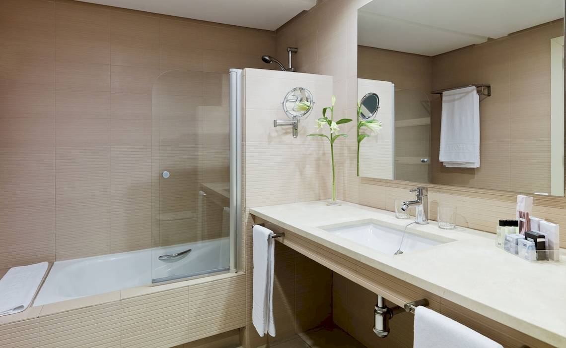 Badezimmer im H10 Estepona Palace mit Badewanne, Waschbecken und Spiegeln.