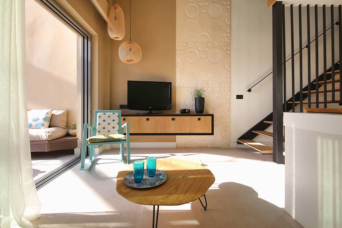 Innenbereich des Domes Noruz Chania, Autograph Collection mit modernem Wohnzimmer, Flachbildfernseher und gemusterter Wand.