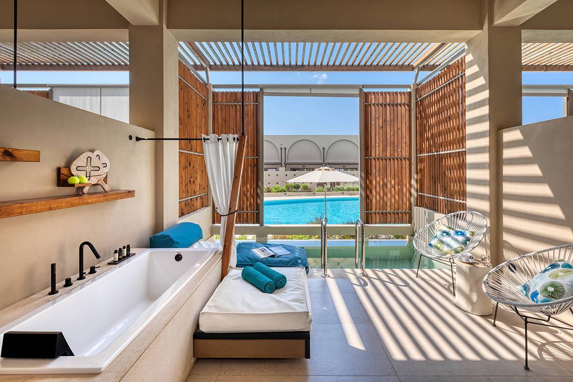 Innenbereich des Domes Noruz Chania, Autograph Collection mit Badewanne, Lounge-Bereich und Pool-Blick.