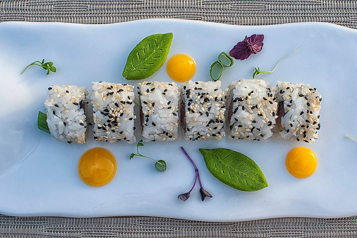 Ein weisses Teller mit verschiedenen Sushi-Rollen, dekoriert mit Eiern und grünen Blättern.