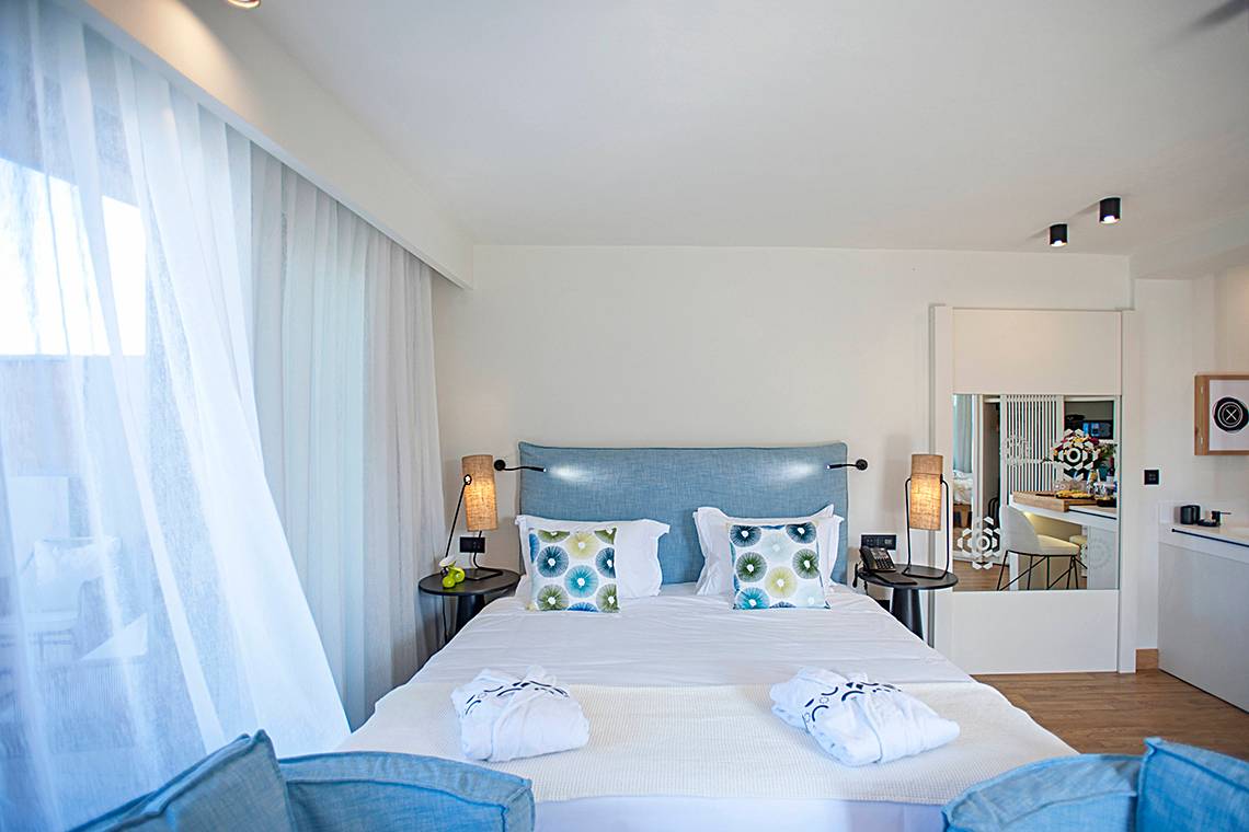 Ein elegantes Hotelzimmer mit einem Doppelbett, zwei Nachttischen und einer gemütlichen Einrichtung im Domes Noruz Chania.