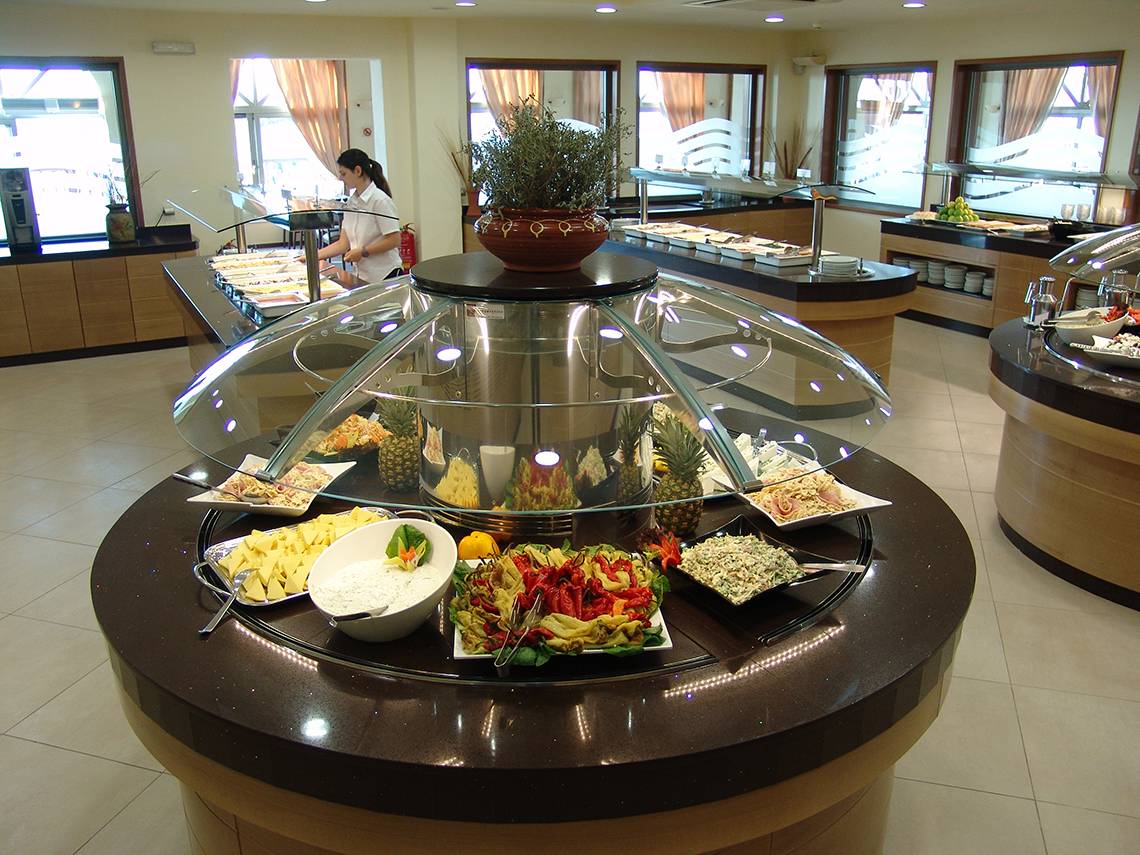 Buffet-Tisch im Europa Beach Hotel mit verschiedenen Gerichten und einer Angestellten im Hintergrund.