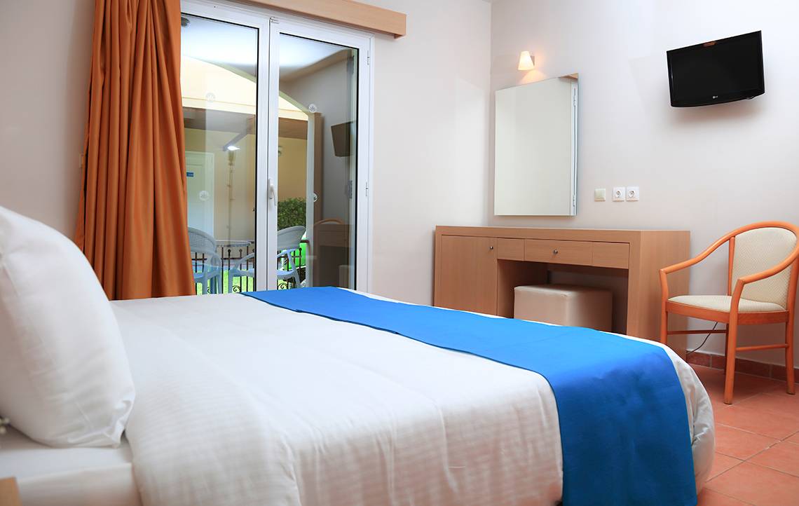 Innenansicht eines Hotelzimmers mit Bett, Nachttisch, Spiegel und Fernseher.