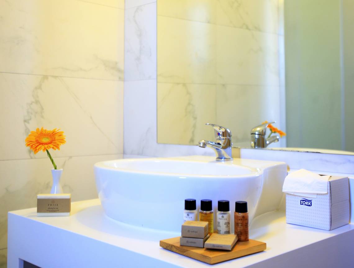 Badezimmer im LABRANDA Marine Aquapark Hotel mit einer weißen Marmorfliesenwand, einem Waschbecken, einer gelben Blume und Pflegeprodukten.