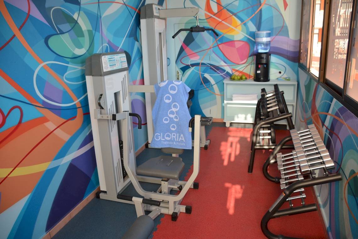 Fitnessstudio im Gloria Palace Amadores Thalasso & Hotel mit bunter Wandgestaltung und Trainingsgeräten.