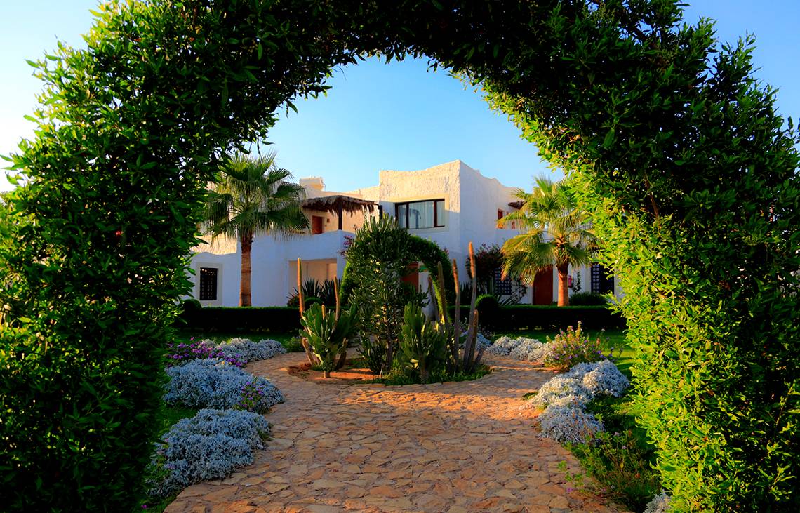 Eingang des Sharm Club Beach Resort mit gepflastertem Weg und grünen Büschen