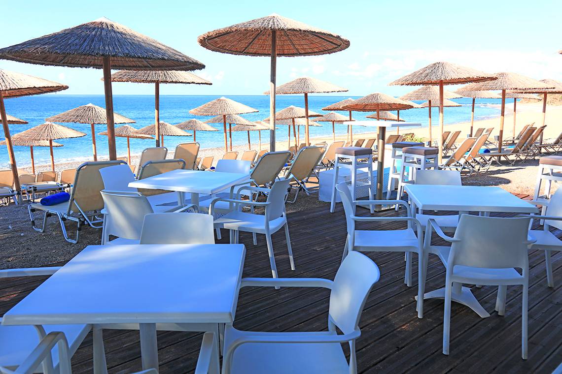 Foto von einer Strandbar mit weißen Stühlen und Sonnenschirmen, Blick auf das Meer.