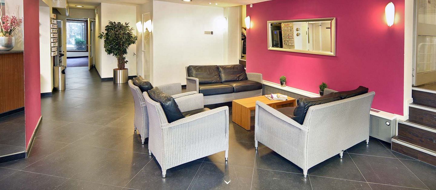 Empfangsbereich des Nova Hotels mit Ledersofas, Tischen und einer rosa Wand.