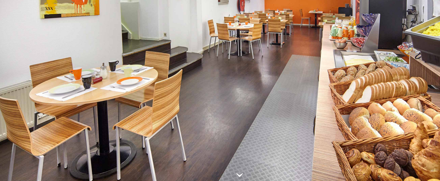Frühstücksraum im Nova Hotel mit Tischen, Stühlen und Frühstücksbuffet.