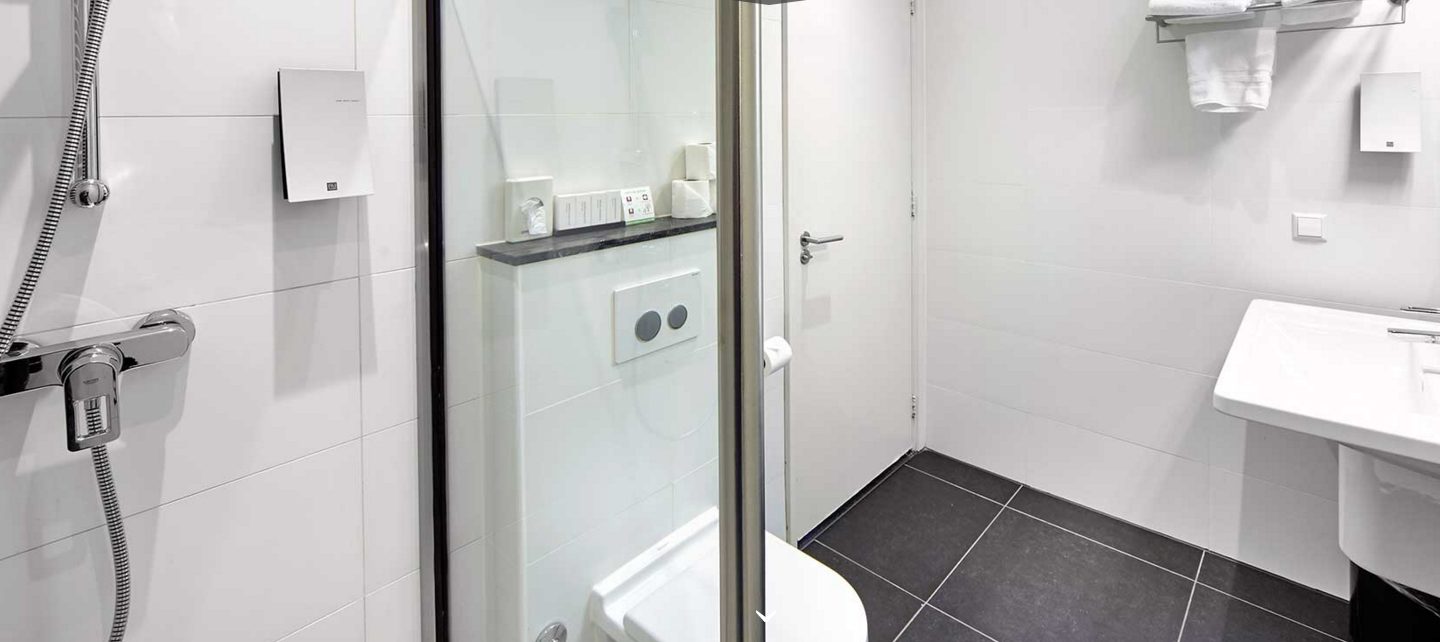 Das Badezimmer im Nova Hotel mit einer Dusche, Toilette, Waschbecken und Fliesenboden.