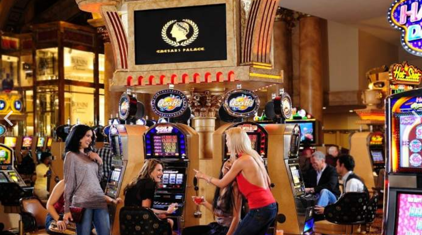 Mehrere Frauen spielen an Spielautomaten in Caesars Palace, mit dem Hotelnamen im Hintergrund.