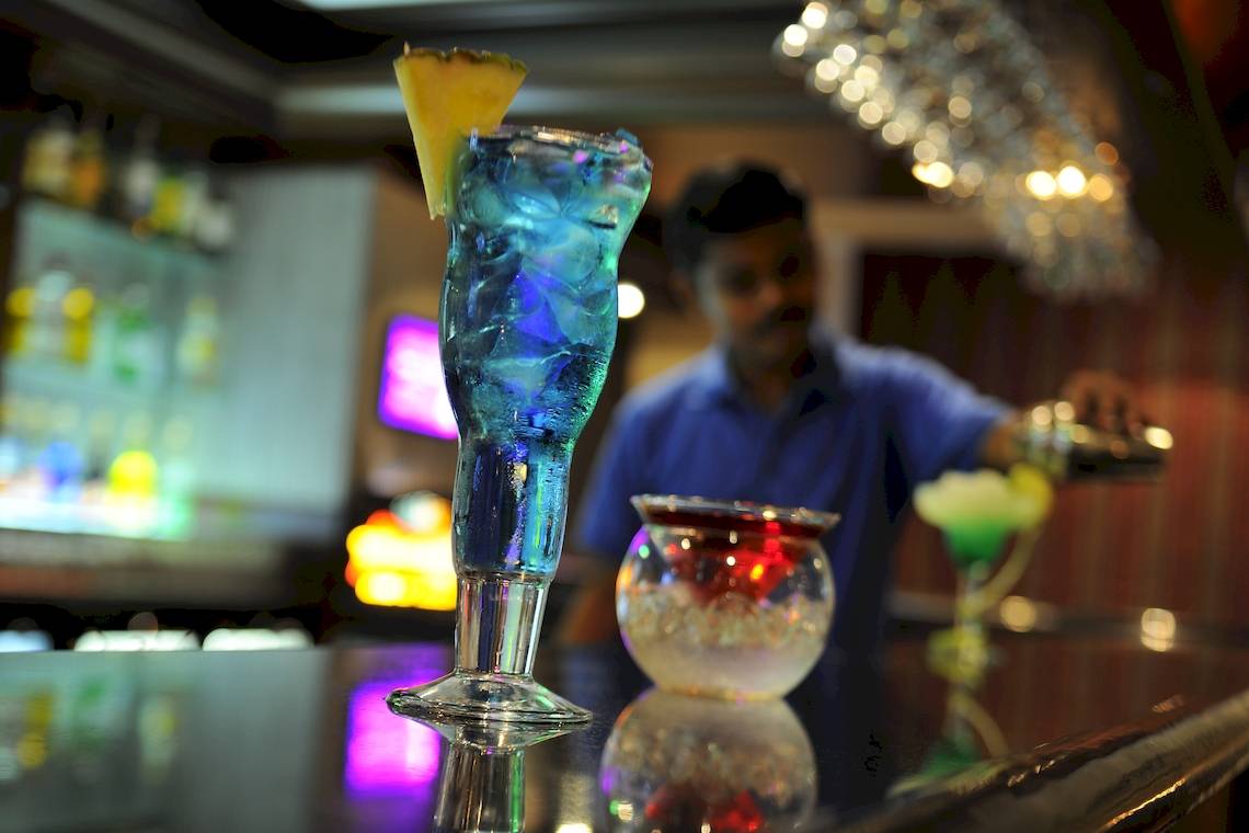 Ein Barkeeper bereitet Cocktails im Wyndham Garden Salalah Mirbat zu, mit einem blauen Cocktailglas und einer Glasvase auf dem Tresen.