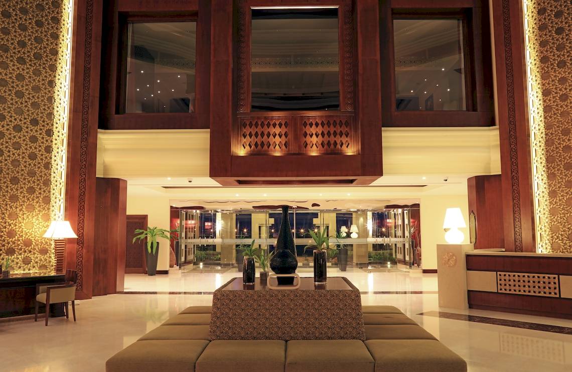 Eingangsbereich des Wyndham Garden Salalah Mirbat Hotel mit Empfang, Sofas und Pflanzen.
