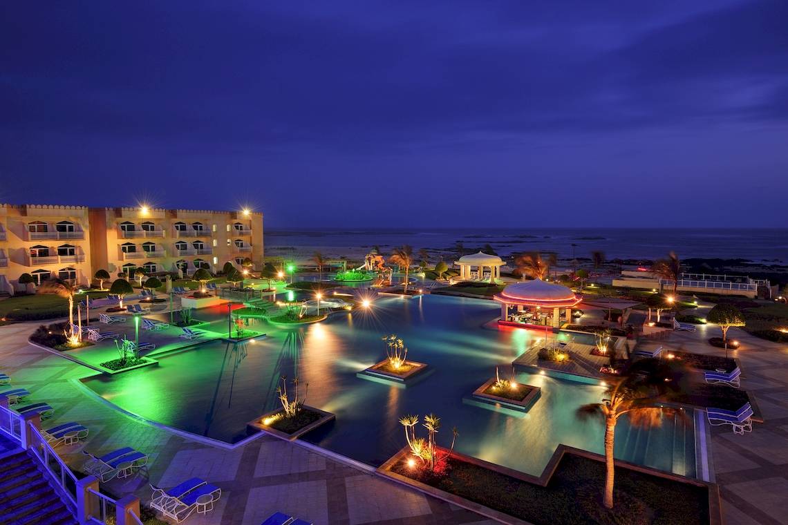 Abendlicher Poolbereich im Wyndham Garden Salalah Mirbat Hotel mit beleuchteten Wasserpflanzen und Lounge-Stühlen.