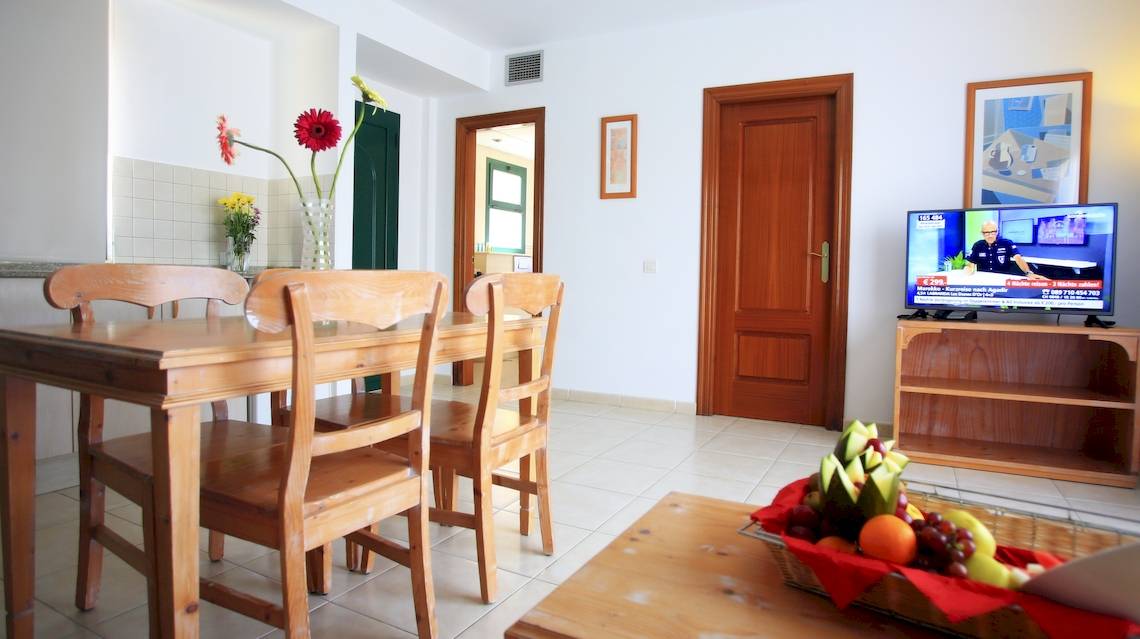 Wohnzimmer des Bluesea Aloe Corralejo Hotels mit Tisch, Stühlen und Fernseher.