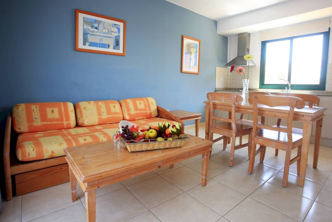 Wohnzimmer im BLUESEA Aloe Corralejo Hotel mit orangefarbener Couch und Tisch mit Obstkorb.